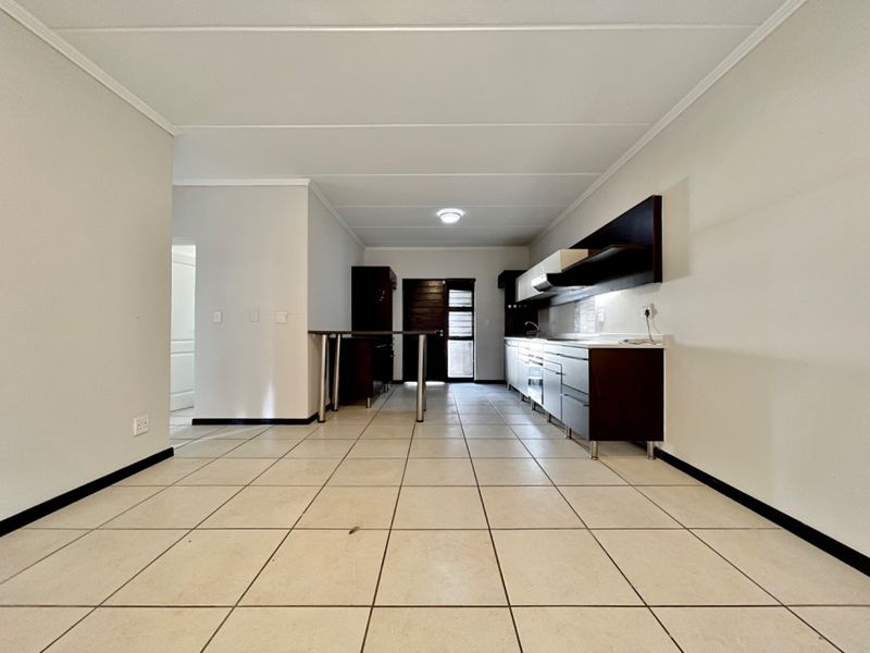 An open-plan kitchen featuring dark cabinetry, a breakfast bar, and tiled flooring, presenting a clean and functional space ready for personalization.