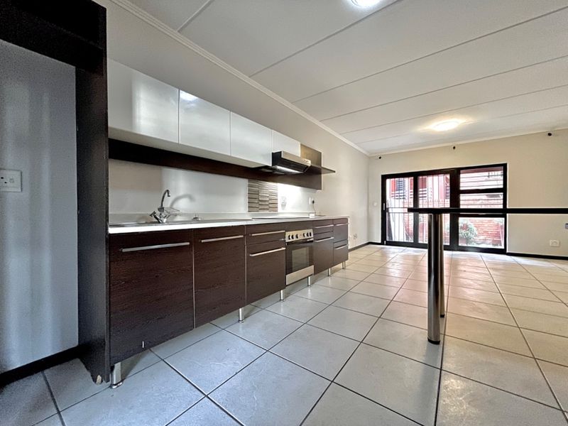 A modern, open-plan kitchen featuring dark wood cabinetry, white upper cabinets, stainless steel appliances, and tiled flooring, leading to an outdoor area.