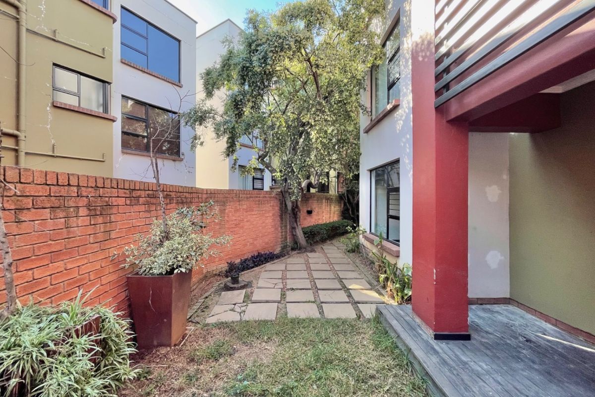 A private rear courtyard featuring a paved walkway, timber decking, and a brick boundary wall, offering a quiet outdoor space for relaxation.