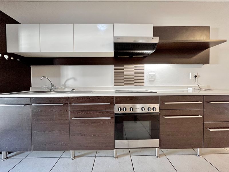 A modern kitchen featuring dark wood-grain lower cabinets, white upper cabinetry, a built-in oven with hob, extractor fan, and tiled flooring.