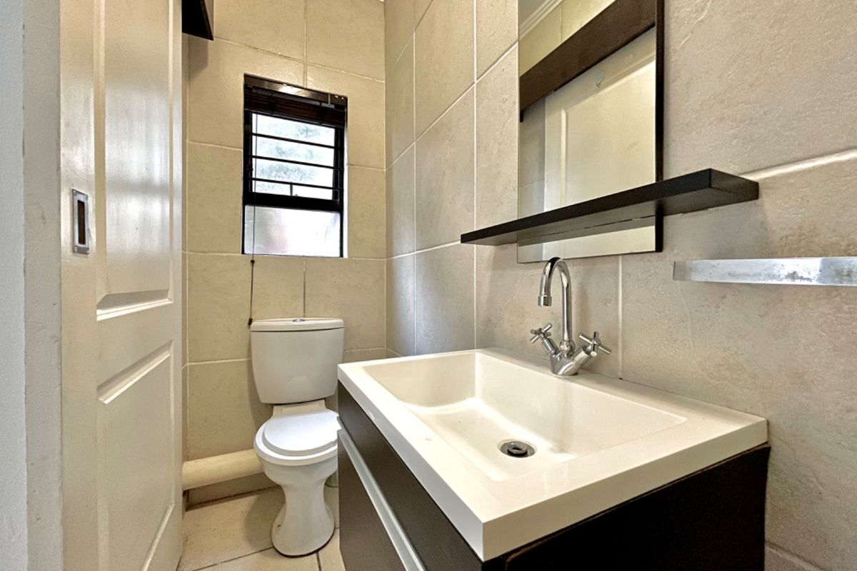 A compact, well-maintained bathroom featuring a modern vanity unit, ceramic basin, wall-mounted mirror, and neutral floor-to-ceiling tiling.