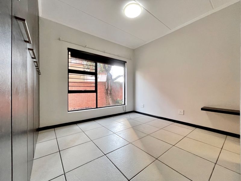 A clean, empty bedroom featuring tiled flooring, built-in cupboards, and a window with security bars.