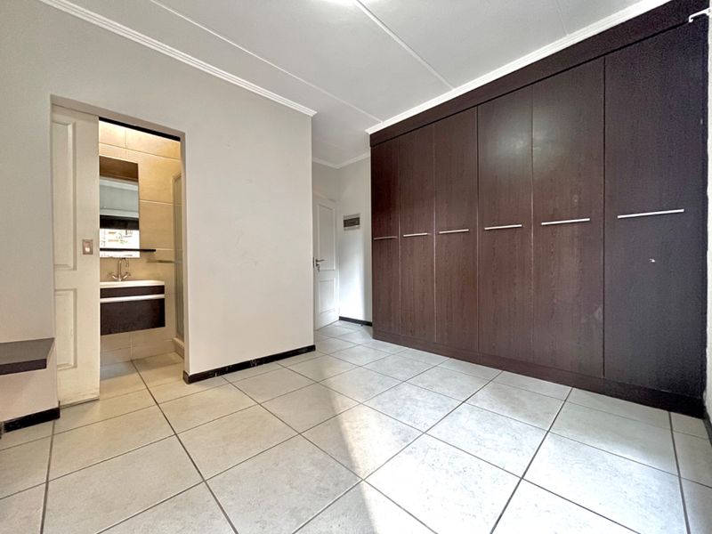 Spacious bedroom featuring large built-in dark wood cupboards, neutral tiled flooring, and direct access to an en-suite bathroom.