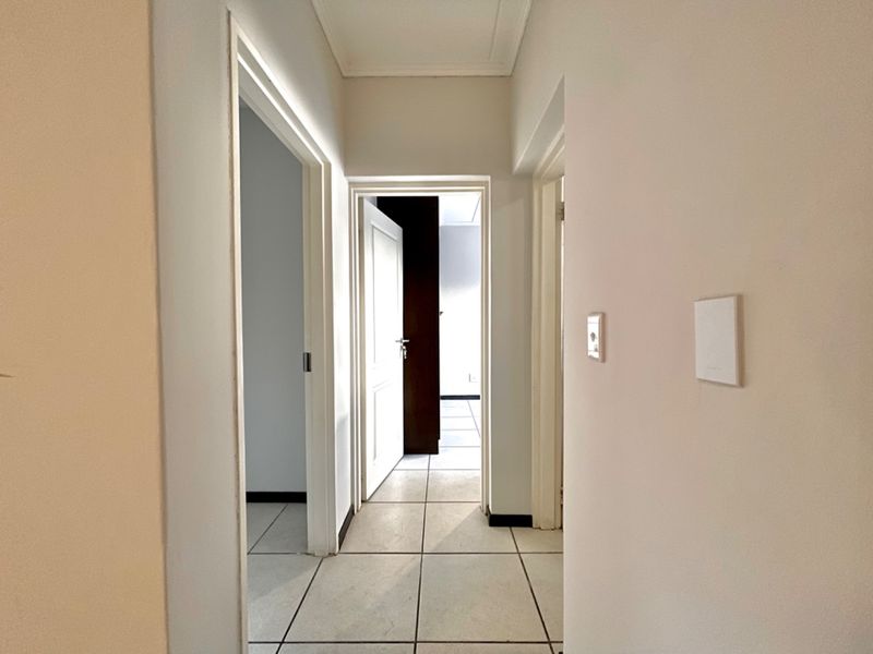 A clean, neutral hallway featuring tiled flooring and multiple internal doorways leading to adjacent rooms.