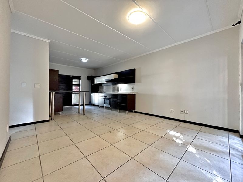 An open-plan kitchen and living area featuring tiled flooring, modern built-in cabinetry, and a breakfast bar, offering a clean and functional space.