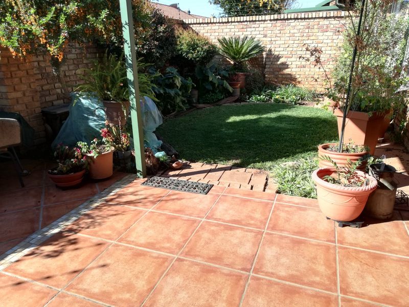A private outdoor patio area featuring terracotta tiling, a small lawn, and a brick boundary wall, providing a cozy space for outdoor relaxation.