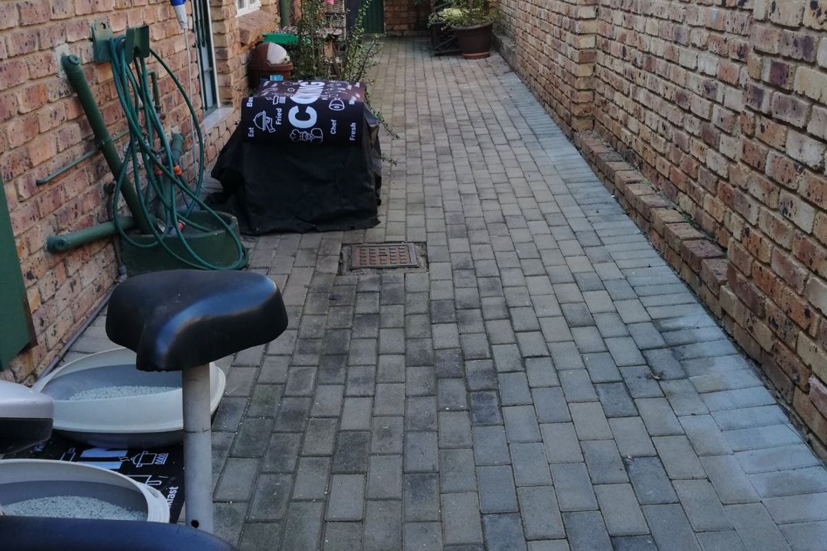 A narrow paved side courtyard or rear walkway featuring exposed brick walls and functional outdoor utility space.