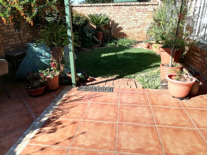 A private outdoor patio area featuring terracotta-style tiling, enclosed by a brick boundary wall and a small landscaped garden section.