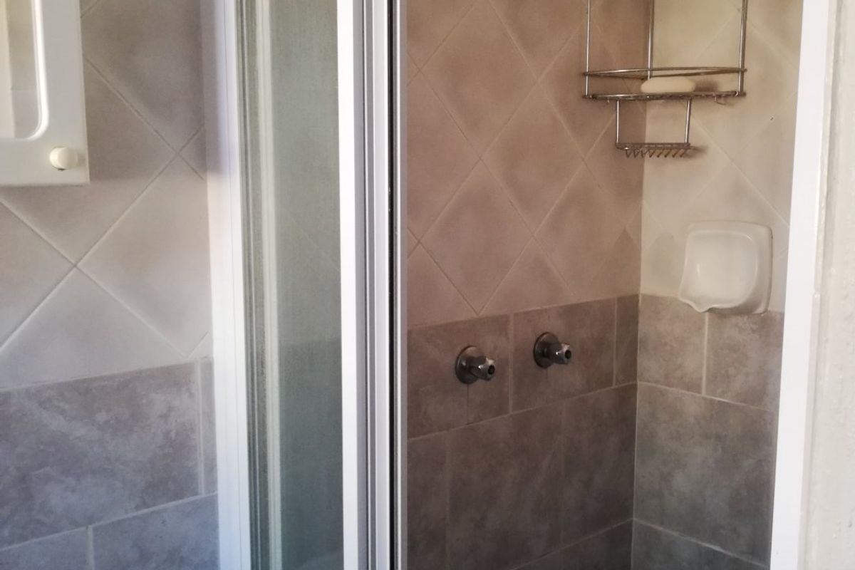 A functional bathroom featuring a tiled shower enclosure with a fixed shower head and a wall-mounted wash basin.
