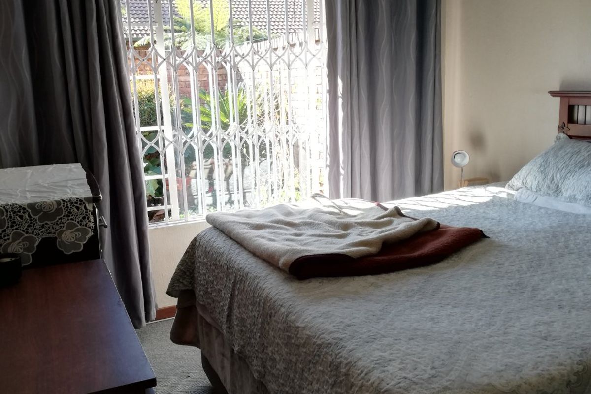A bedroom featuring carpeted flooring, a ceiling fan, and a window fitted with a security gate and curtain rails.
