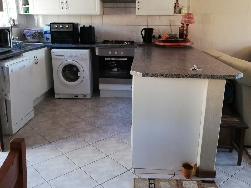 Open plan kitchen featuring white cabinetry, laminate countertops, a breakfast bar, and integrated gas hob with extractor fan, finished with tiled flooring.