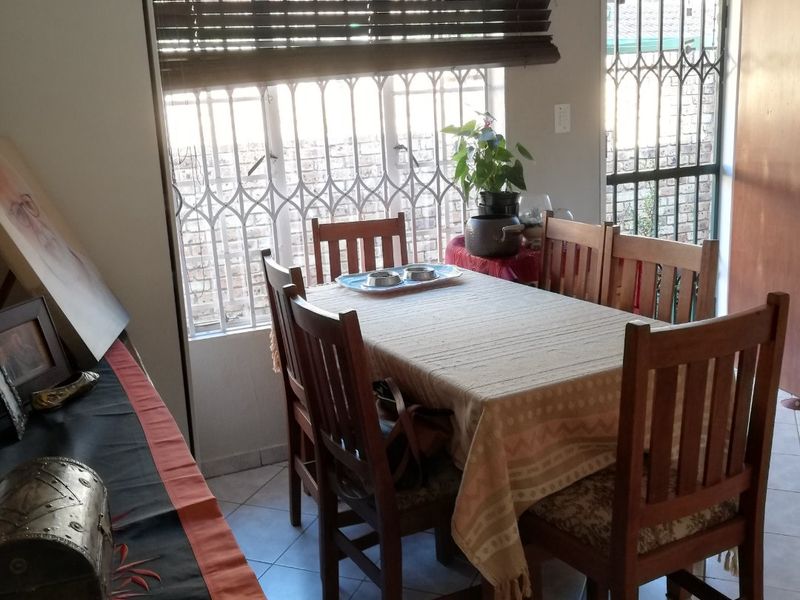 A functional dining area featuring tiled flooring, security gates on windows and doors, and venetian blinds, providing a secure and practical space.