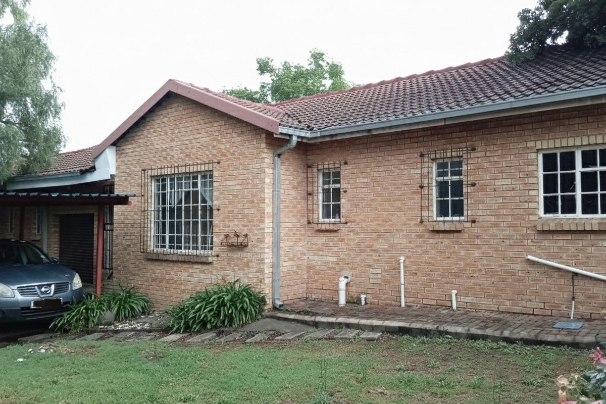 Rear view of a face brick apartment building featuring a tiled roof, security bars on windows, and an attached carport.
