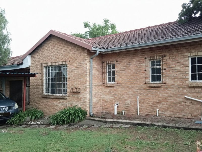 Rear view of a face brick apartment building featuring a tiled roof, security bars on windows, and an attached carport.