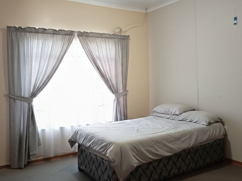 A bedroom featuring neutral walls, carpeted flooring, and window treatments. The space requires minor cosmetic updates and electrical finishing.
