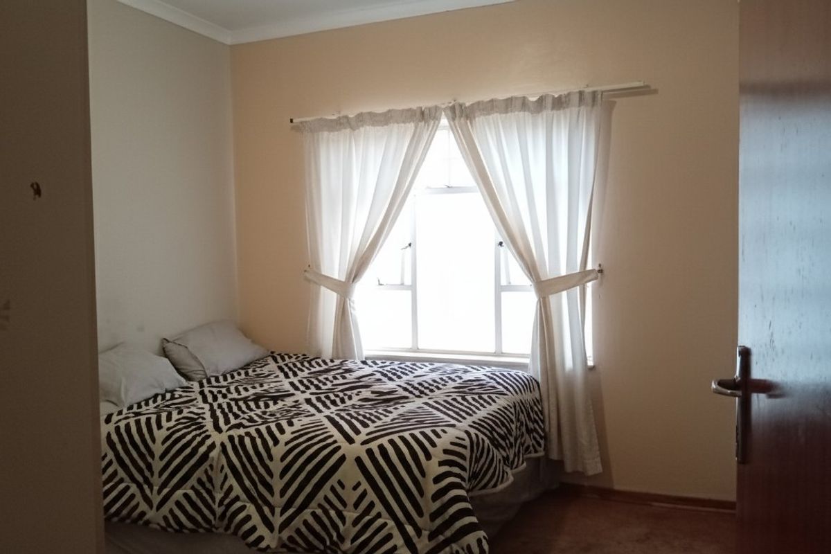 A standard bedroom featuring a window with curtains and a wooden door, providing a functional living space.