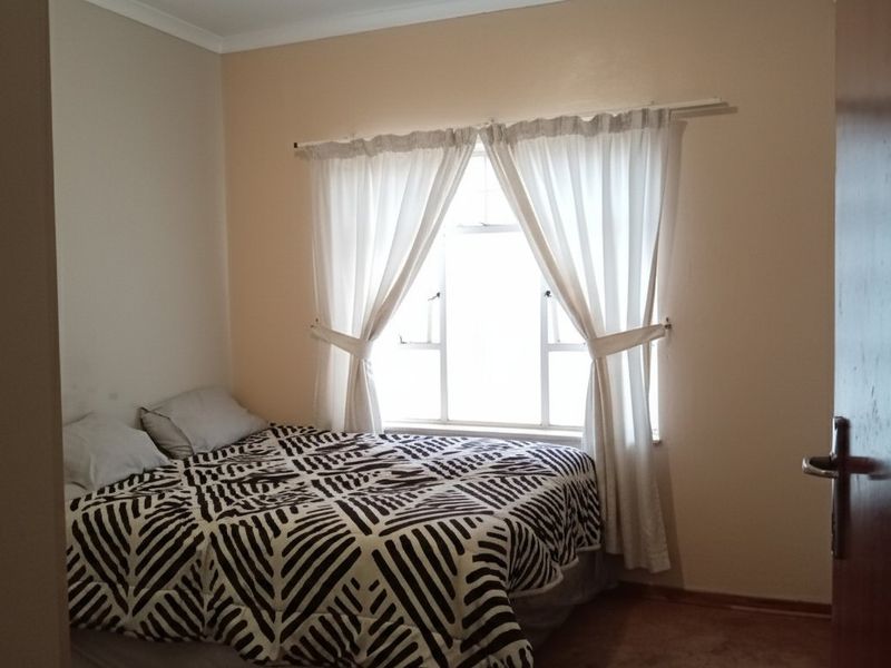 A standard bedroom featuring a window with curtains and a wooden door, providing a functional living space.