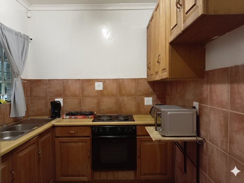 A functional kitchen featuring wooden cabinetry, a built-in oven with electric hob, and a double bowl sink with tiled backsplash.