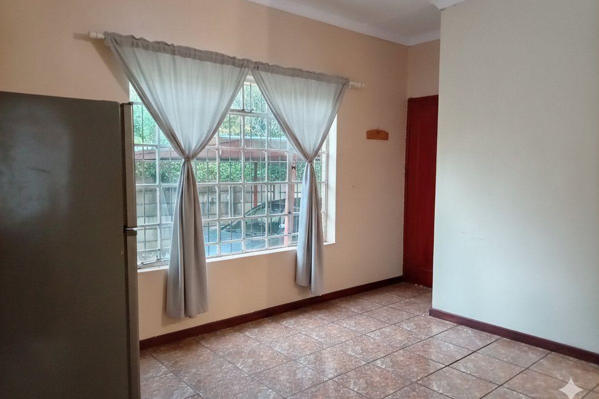 A simple, empty living area featuring tiled flooring and a large window with security bars, offering a neutral canvas for personalization.