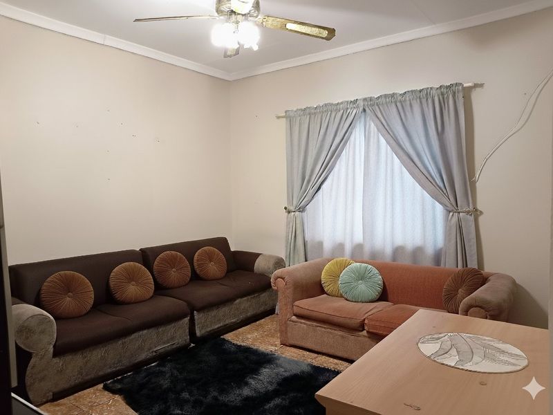 A living room featuring tiled flooring and a ceiling fan, requiring minor cosmetic updates to the walls and electrical fixtures.