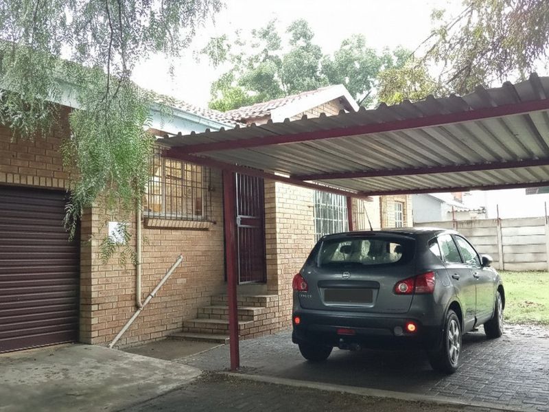 Front exterior view of the apartment featuring a brick facade, a covered carport, and a paved driveway area.