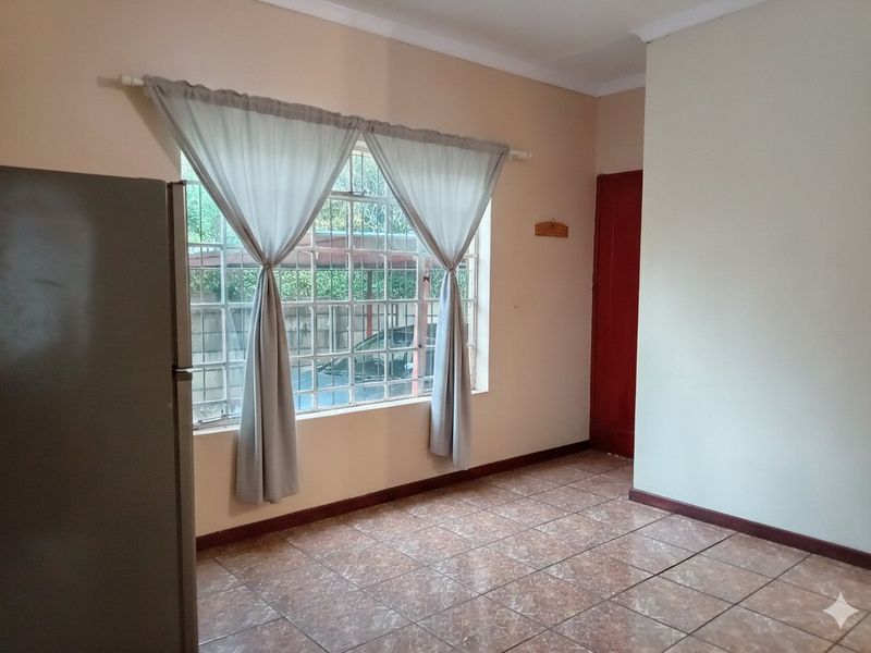 A simple, empty living area featuring tiled flooring and a large window with security bars, offering a neutral canvas for personalization.