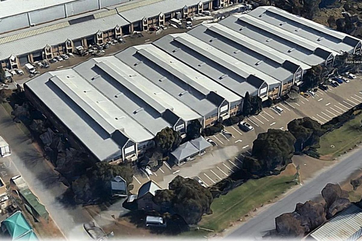 Aerial view of an industrial warehouse complex featuring extensive metal roofing, dedicated parking bays, and surrounding landscaped areas.