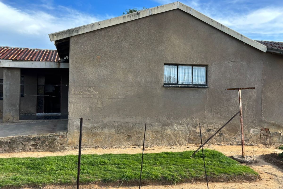 Rear view of the property showing plastered exterior walls, tiled roofing, and metal-framed windows with security bars, requiring maintenance and exterior refurbishment.