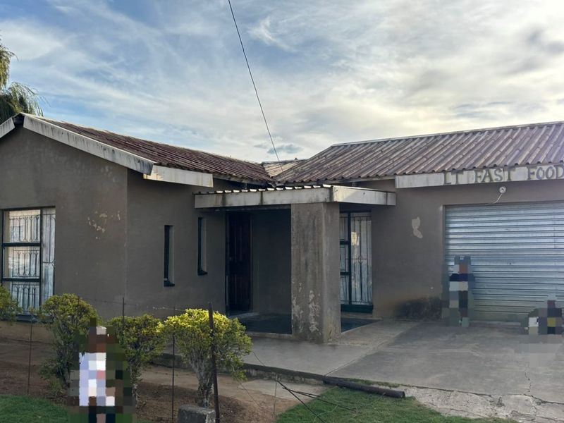 Front elevation of a single-story house featuring a tiled roof, covered entrance, and a metal roller garage door, showing signs of exterior wear.