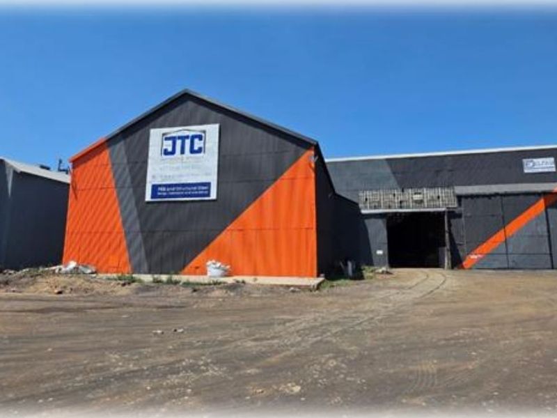 Industrial warehouse facility featuring large sliding doors, metal cladding, and a spacious unpaved yard area suitable for heavy vehicle access.