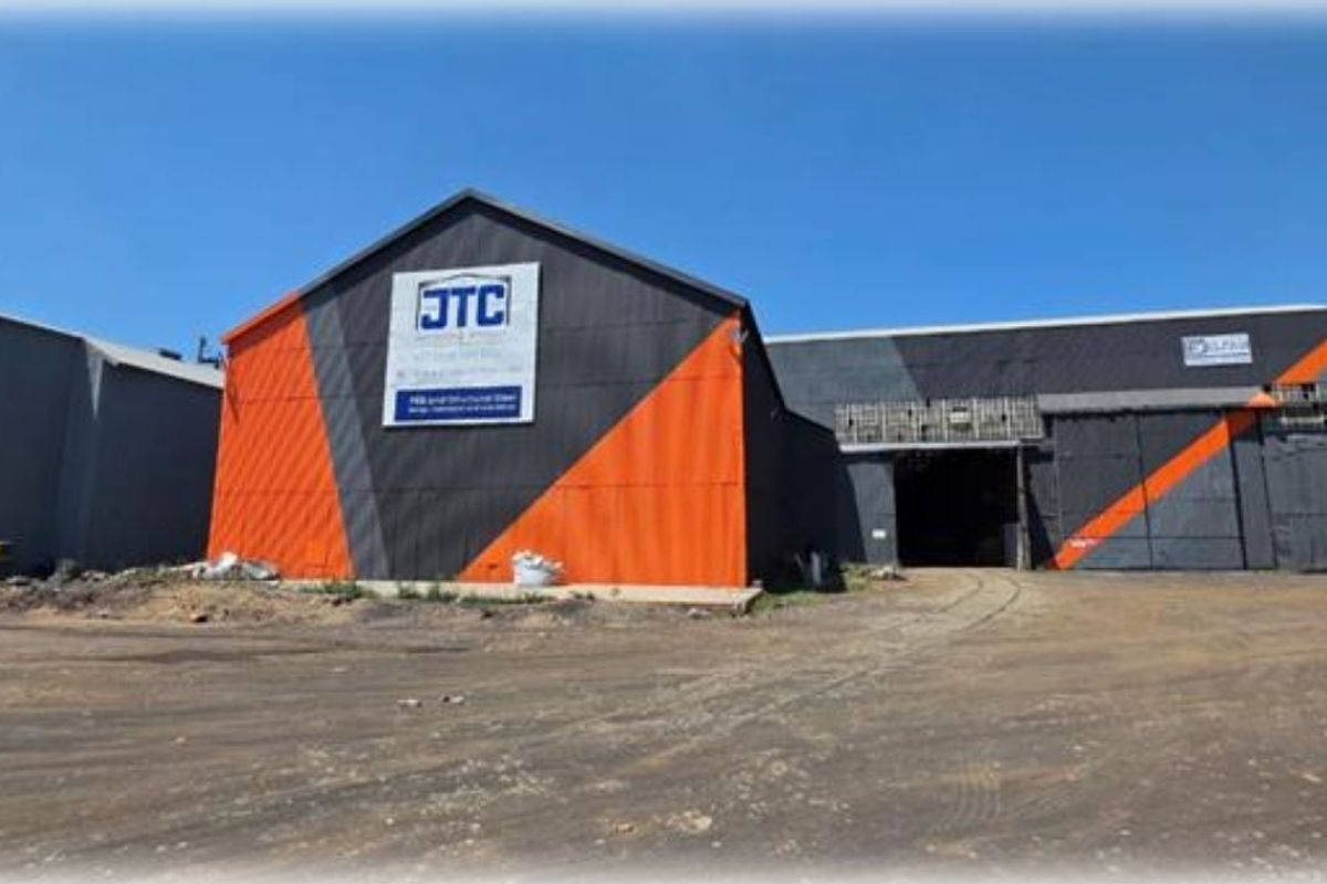 Industrial warehouse facility featuring large sliding doors, metal cladding, and a spacious unpaved yard area suitable for heavy vehicle access.