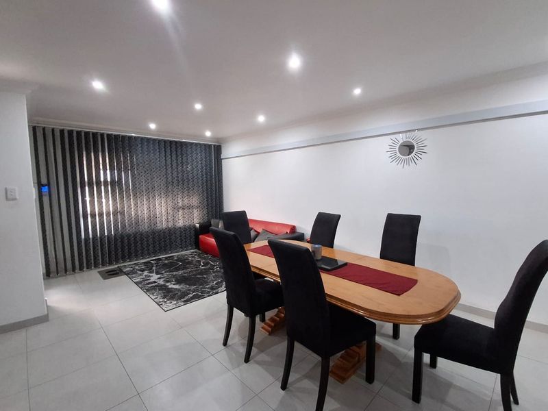 Open plan living and dining area featuring neutral tiled flooring, recessed downlighting, and modern vertical window blinds.