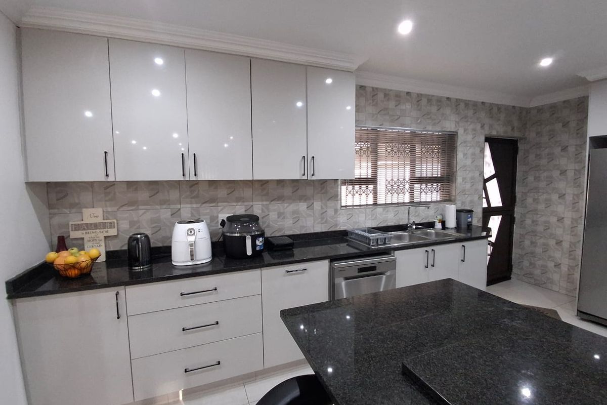 Modern kitchen featuring high-gloss cabinetry, granite countertops, a central island, and integrated appliances, offering a clean and functional culinary space.