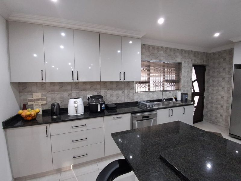 Modern kitchen featuring high-gloss cabinetry, granite countertops, a central island, and integrated appliances, offering a clean and functional culinary space.