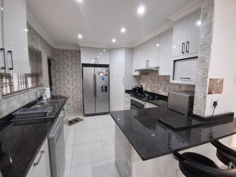 Modern kitchen featuring granite countertops, high-gloss cabinetry, gas hob, extractor fan, and tiled finishes throughout.