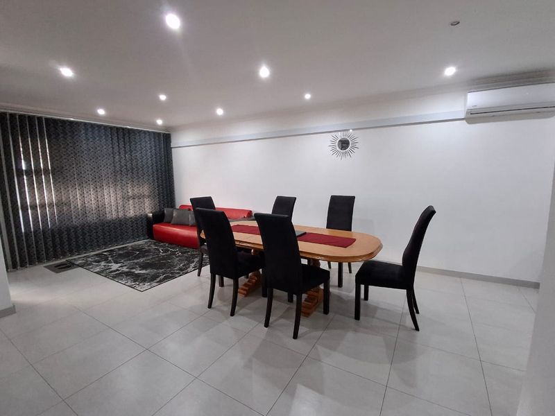 Spacious dining area featuring neutral tiled flooring, recessed downlighting, and a wall-mounted split-system air conditioner for climate control.