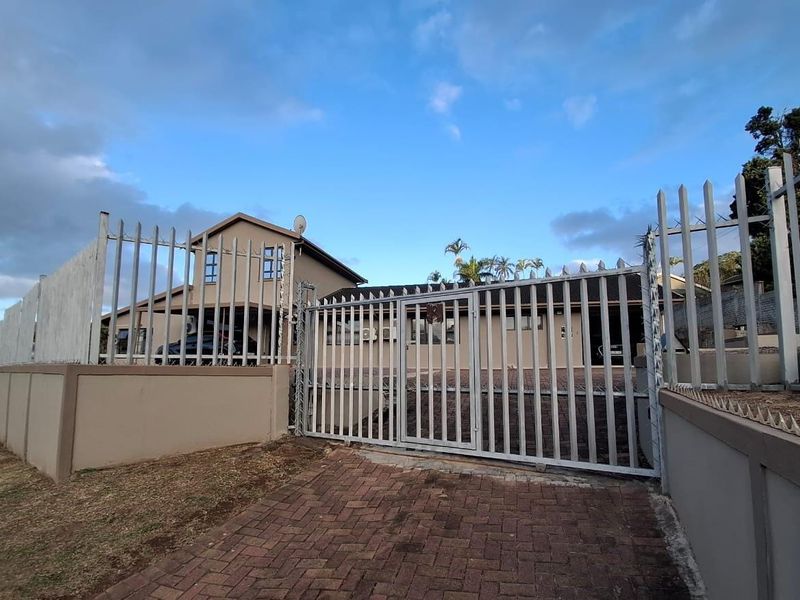 Front view of the property featuring a paved driveway, secure steel gate, and perimeter fencing with spiked security topping.
