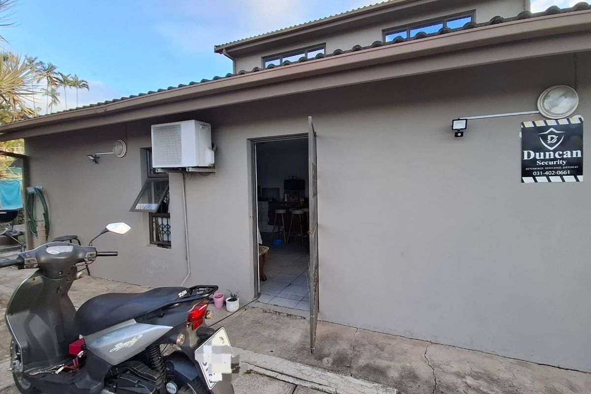 Rear exterior view of the property featuring a security gate, mounted air conditioning unit, and concrete paving.