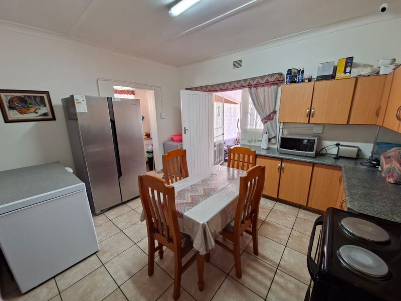 A functional kitchen featuring laminate cabinetry, tiled flooring, and an electric stove, with an adjacent dining area and access to a rear utility space.