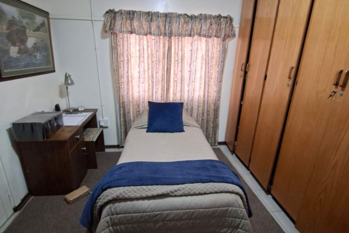A compact bedroom featuring floor-to-ceiling built-in wooden cupboards and a window with a valance.
