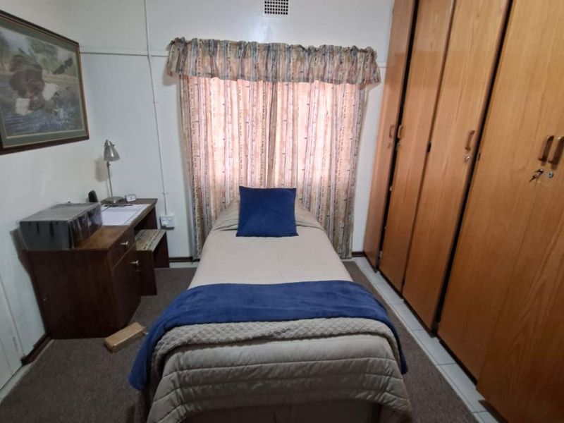 A compact bedroom featuring floor-to-ceiling built-in wooden cupboards and a window with a valance.