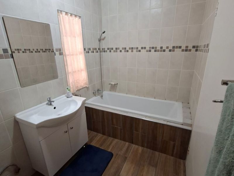 A functional bathroom featuring a built-in vanity, bathtub with shower mixer, and neutral wall tiling with decorative mosaic accents.
