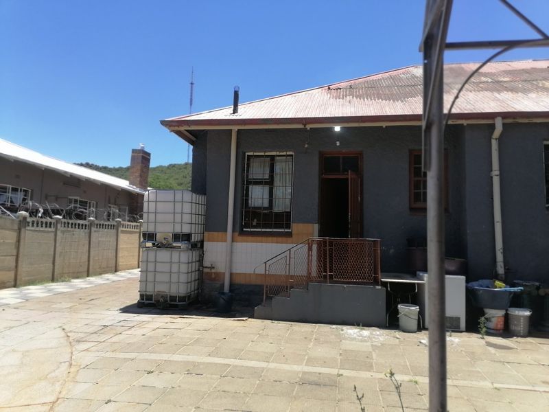 Rear exterior view of the property featuring a paved courtyard, corrugated metal roof, and security-fitted windows and doors.