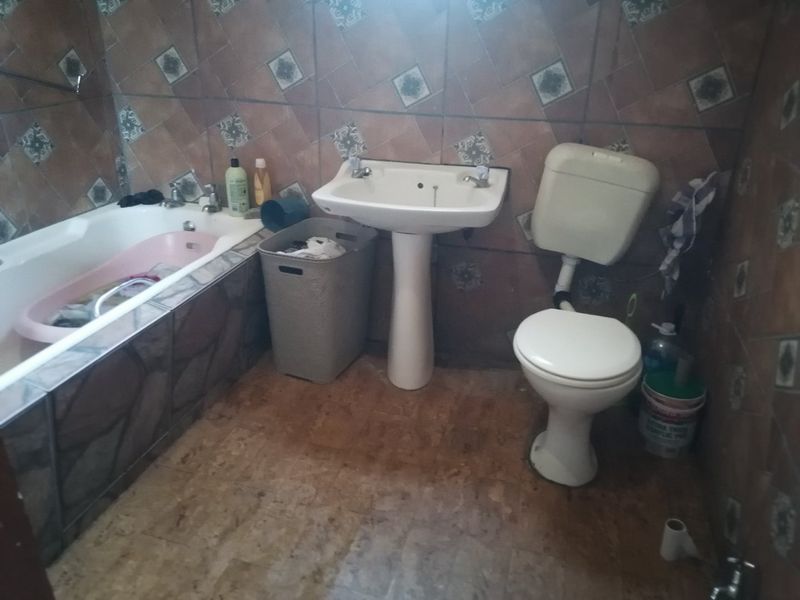 A dated bathroom featuring a pedestal washbasin, toilet, and bathtub with full-height wall tiling and floor tiles.