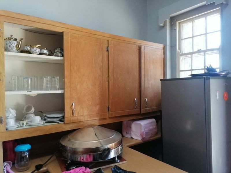 A kitchen area featuring wooden cabinetry and a sash window, showing signs of wear and dated finishes.