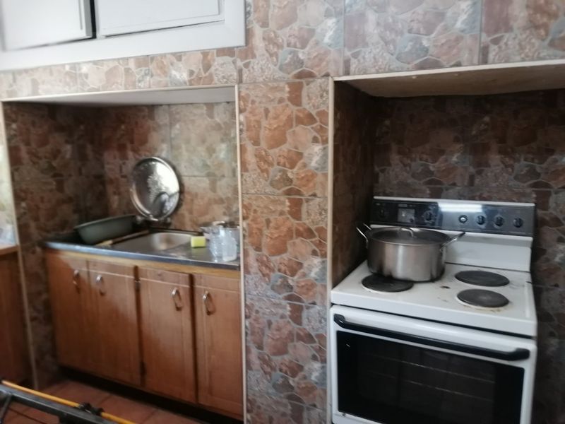 A functional kitchen area featuring built-in wooden cabinetry, a stainless steel sink, and a freestanding electric stove with tiled wall finishes.