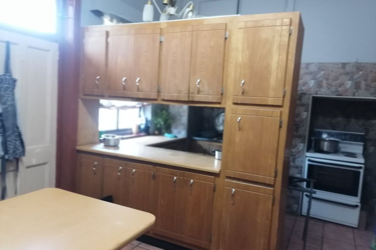 A dated kitchen featuring traditional wooden cabinetry, laminate countertops, and a freestanding oven with tiled flooring and backsplash.