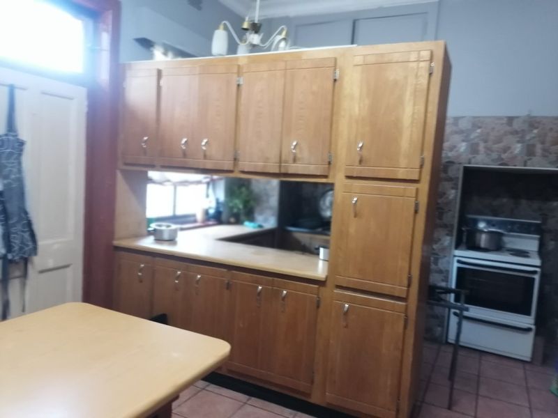 A dated kitchen featuring traditional wooden cabinetry, laminate countertops, and a freestanding oven with tiled flooring and backsplash.