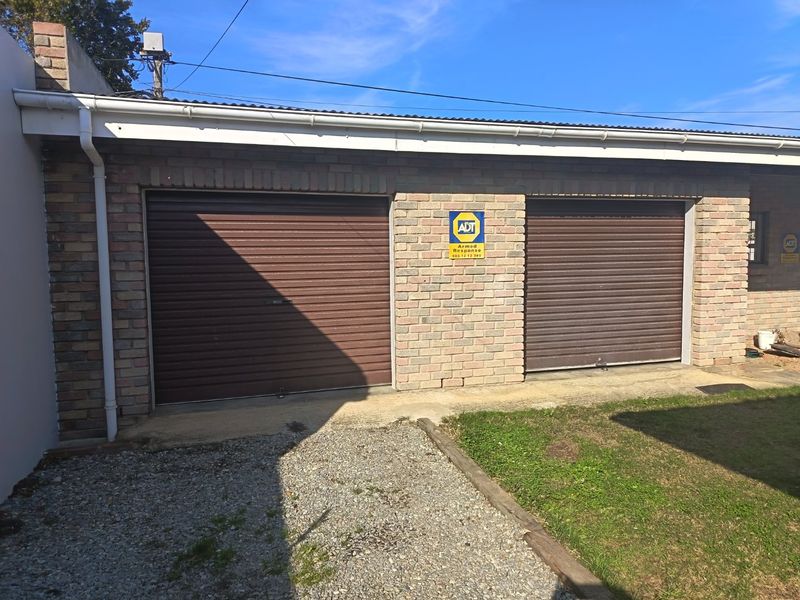 A double garage featuring brown roller doors and face brick construction, equipped with security alarm signage.