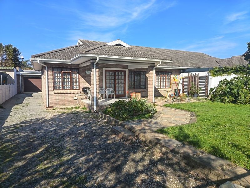 A single-story brick house featuring a covered front patio, tiled roof, paved garden path, and a detached garage with a gravel driveway.